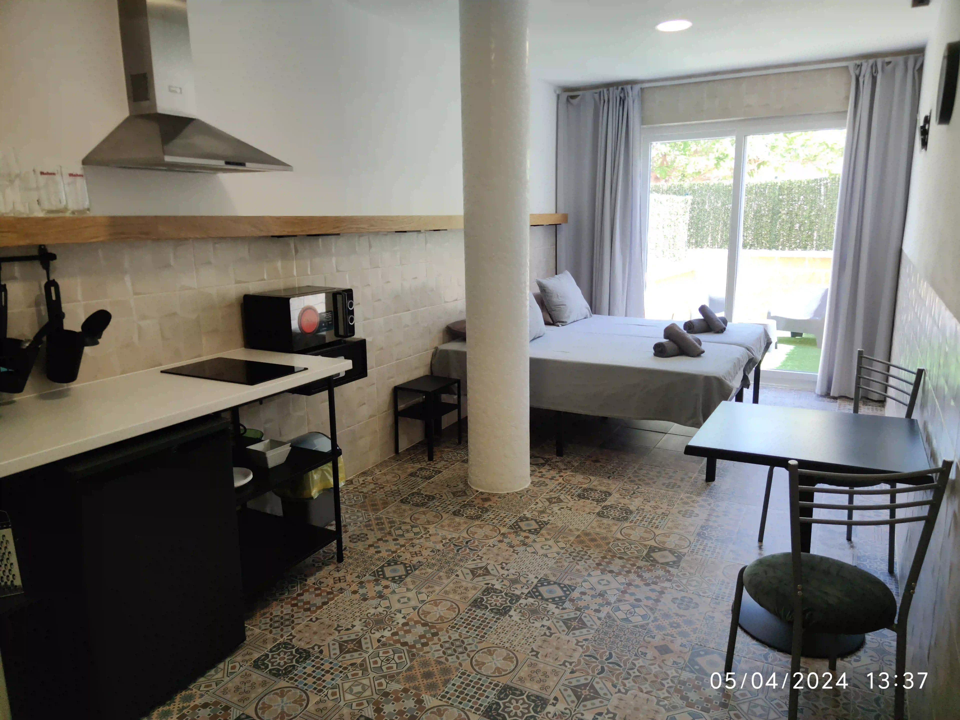 A La Ruta studio seen past its kitchen counter: two single beds by the terrace doors, with the terrace furniture outside