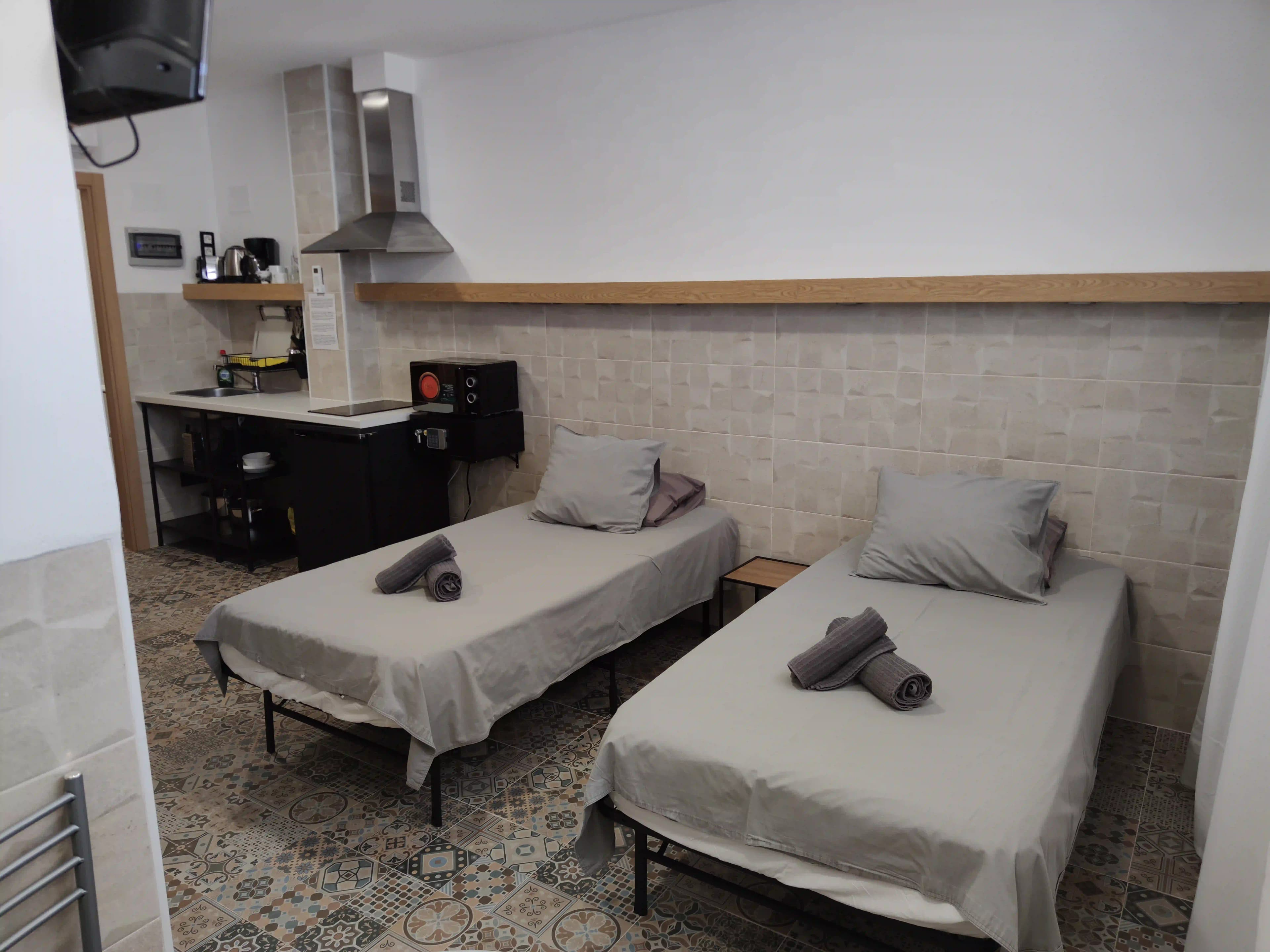 Two single beds in a studio at Hotel Apartamentos La Ruta, with the kitchenette, in-room safe and wall-mounted TV behind them