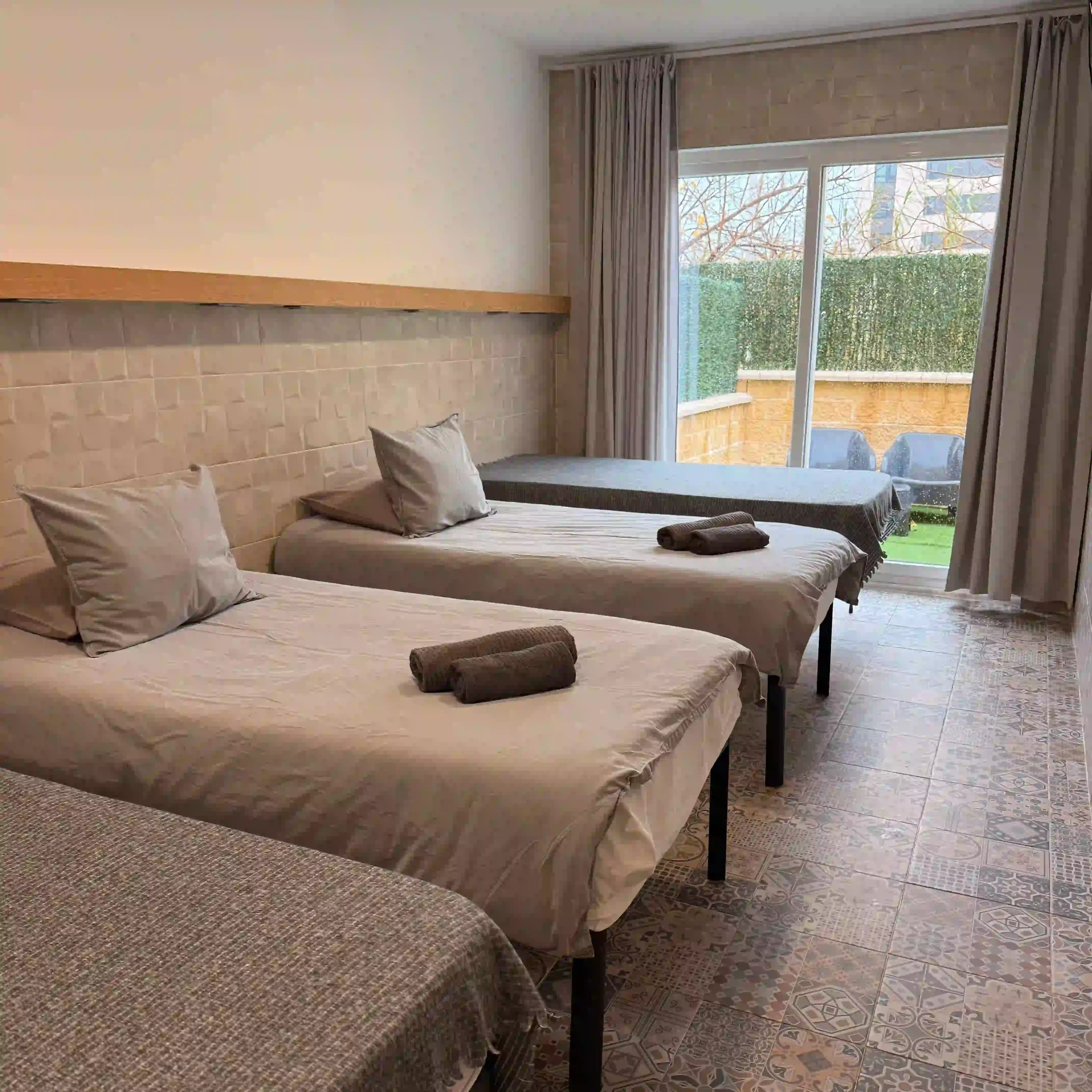 Four single beds in a La Ruta studio, with the private terrace and its seating visible through the window