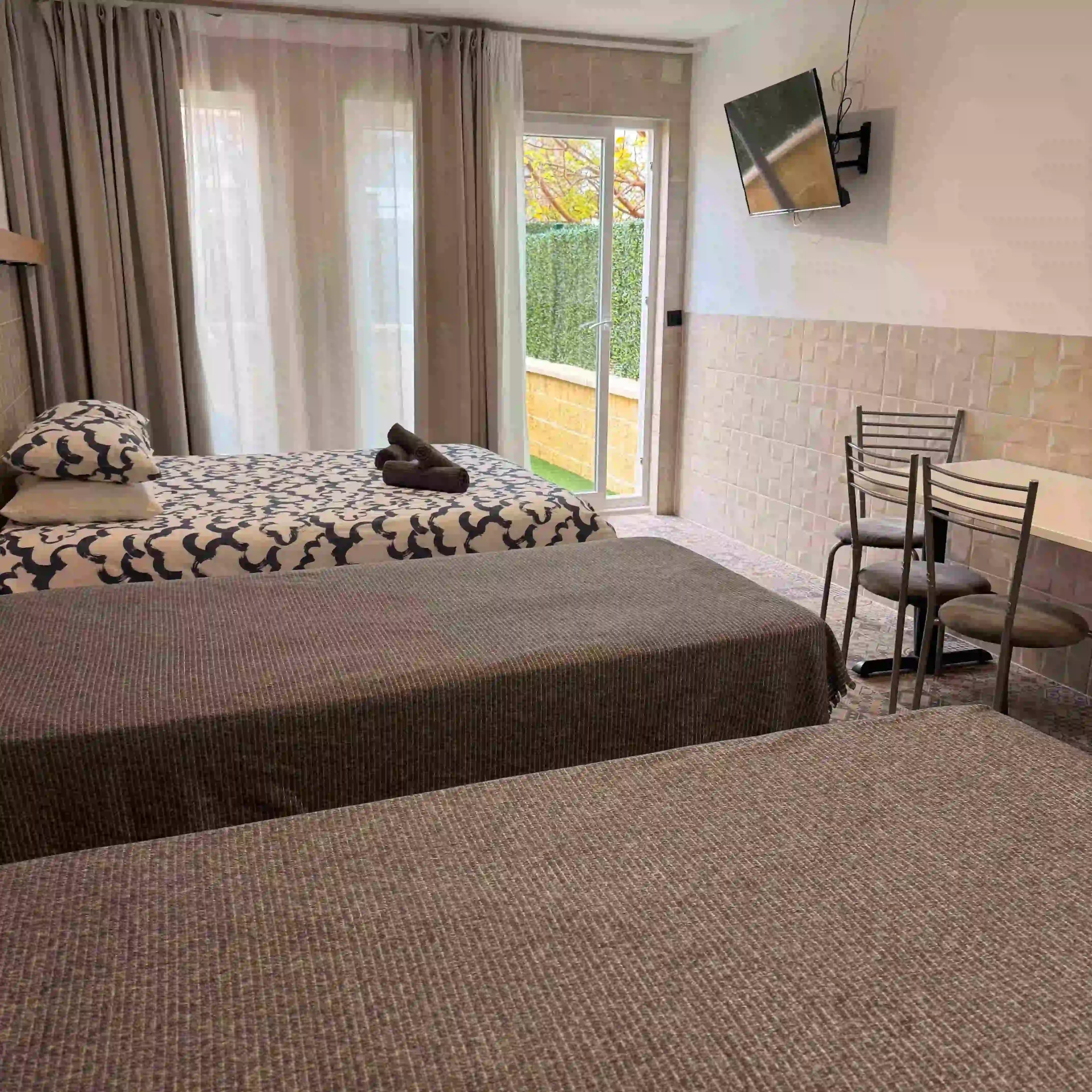 A double bed and two single beds in a La Ruta studio, with a dining table and the garden door beside them