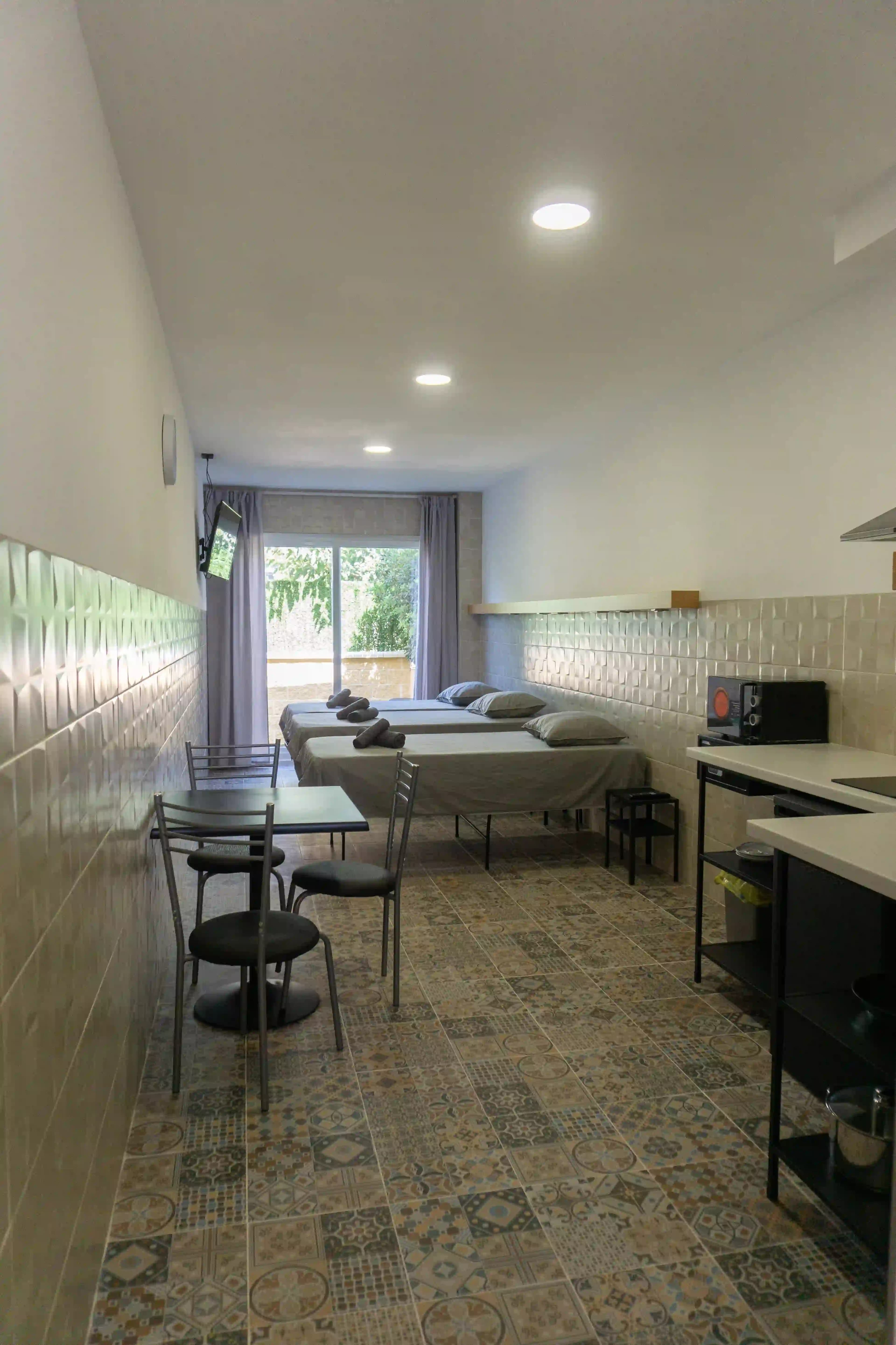Three single beds along the wall of a La Ruta studio, with a dining table, a kitchenette and the terrace doors at the far end