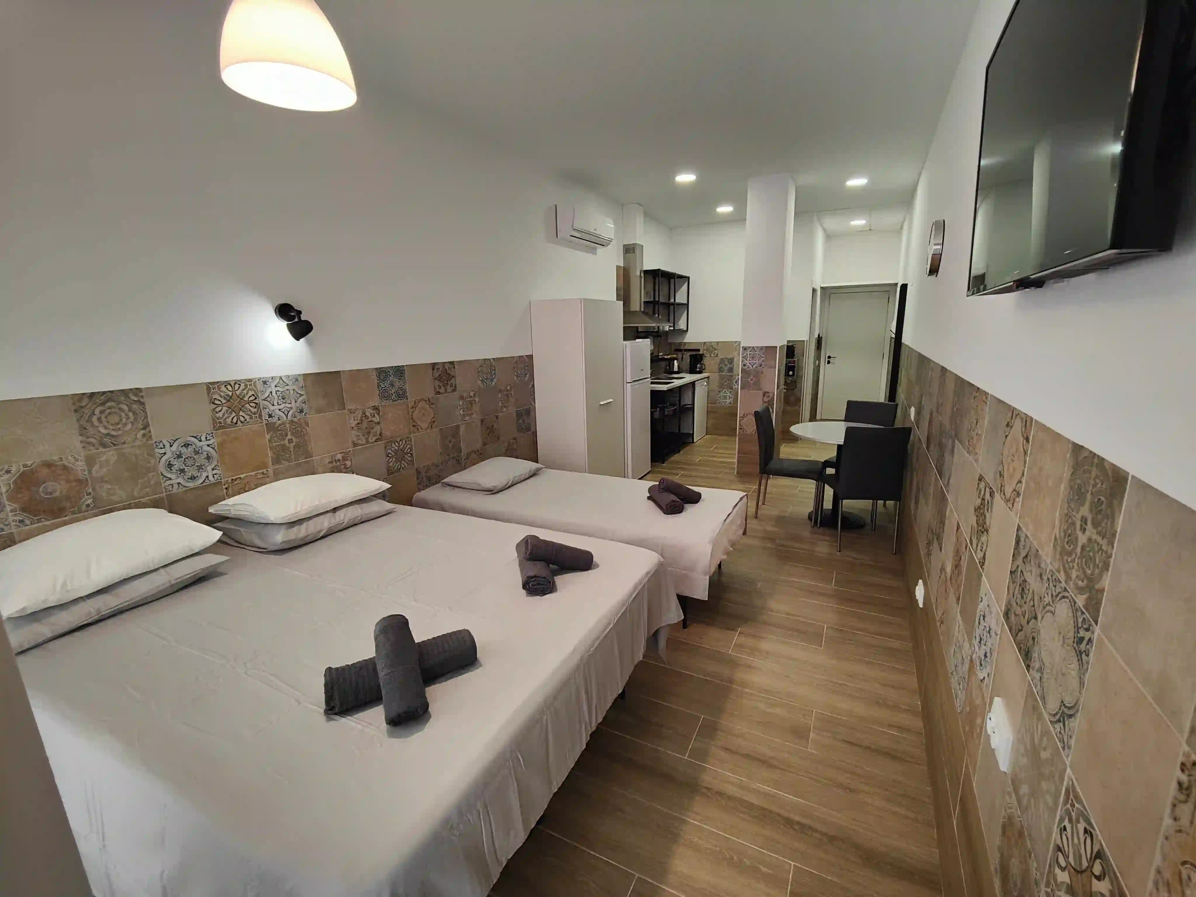 A double bed and a single bed in a Pueblo Mar studio, with the dining table and kitchenette at the far end